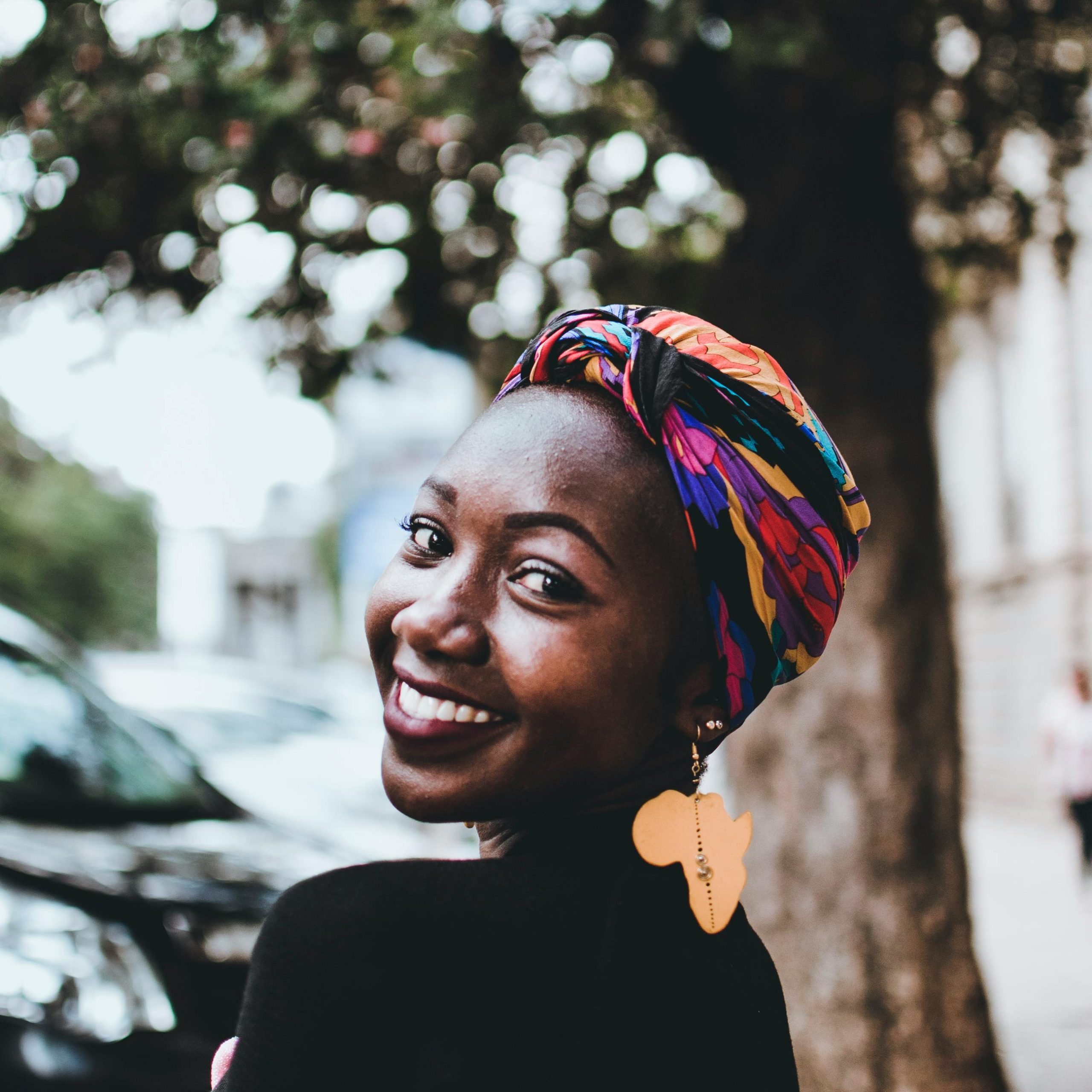 Beautiful portrait of a smiling African woman wearing a vibrant headscarf and earring outdoors in an urban setting.